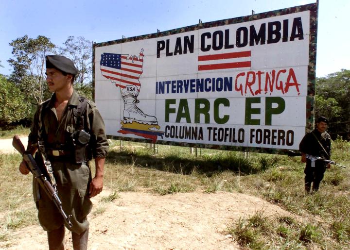 SAN VICENTE, COLOMBIA: Two guerrillas of the Revolutionary Armed Forces of Colombia (FARD) stand guard on a highway next to a billboard with propaganda against the US-backed Colombia Plan in San Vicente, Colombia 30 January 2001. AFP PHOTO/Luis ACOSTA (Photo credit should read LUIS ACOSTA/AFP/Getty Images)