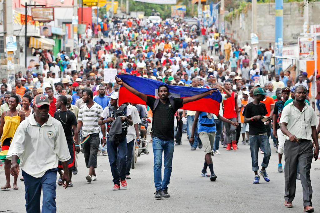 Asistente a una marcha pacífica en Haití sostiene a sus espaldas la bandera de su país 